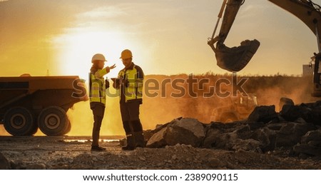 Cinematic Golden Hour Shot Of Construction Site: Caucasian Male Civil Engineer And Hispanic Female Urban Planner Talking, Using Tablet. Trucks, Excavators, Loaders Working To Build New Apartment Block Royalty-Free Stock Photo #2389090115