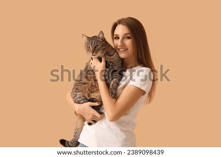 Pretty young woman with cute tabby cat on beige background