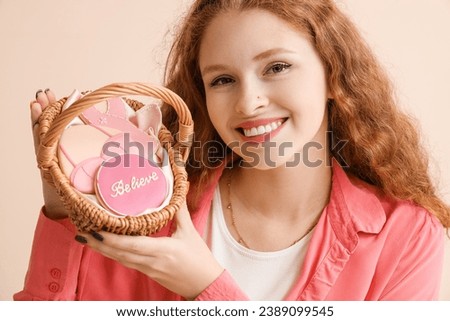 Young woman with basket of cookies on beige background, closeup. Breast cancer awareness concept
