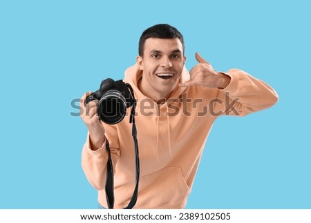 Male photographer with camera showing "call me" gesture on blue background