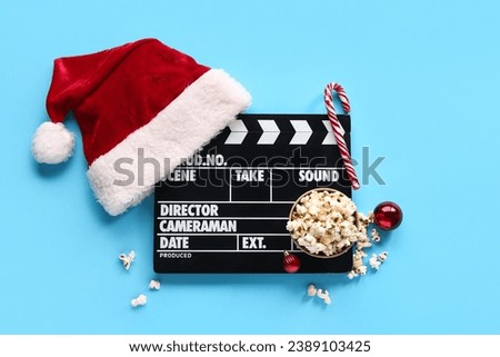 Movie clapper with Santa Claus hat and popcorn on blue background
