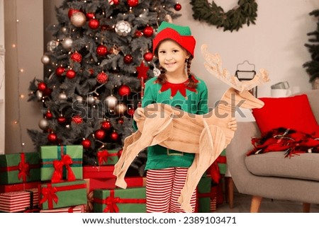 Cute little girl in elf costume with wooden reindeer at home on Christmas eve