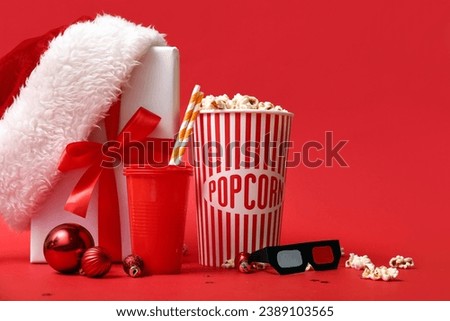 Bucket of popcorn with drink, 3D glasses and Christmas decor on red background