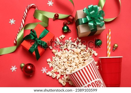 Bucket of popcorn with cup, gifts and Christmas decor on red background