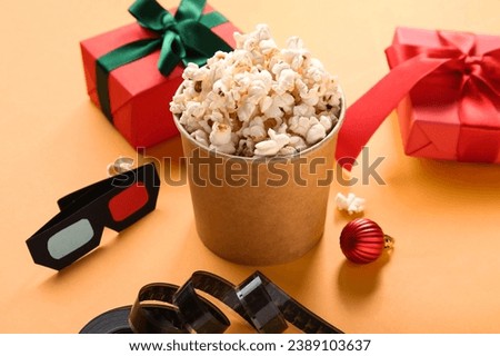 Bucket of popcorn with film reel, 3D glasses and gifts on orange background