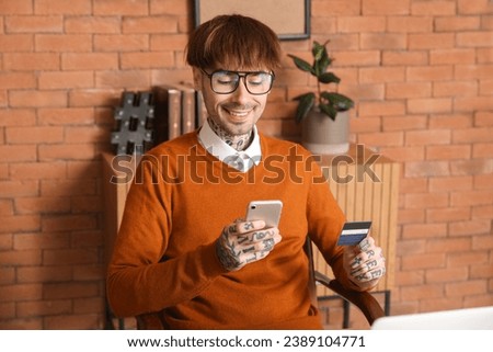 Young man with credit card using mobile phone in office