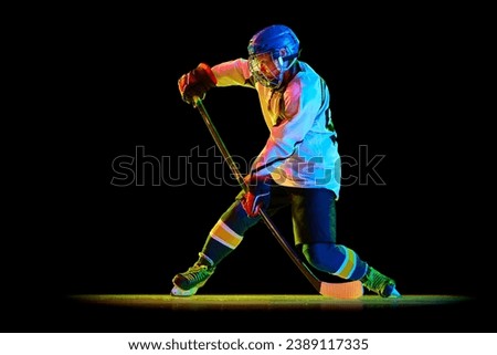 Young woman, professional hockey player in motion, training, playing against black studio background in neon light. Success. Concept of professional sport, competition, game, action, hobby