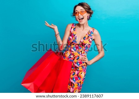 Photo of funky woman with bob hair dressed colorful clothes hold new outfit palm demonstrate empty space isolated on blue color background