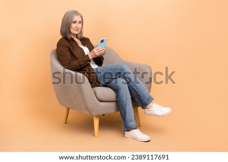 Full body size photo of sitting comfort armchair retired businesswoman browsing candidates list phone isolated over beige color background