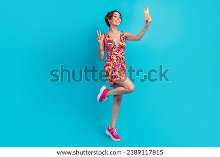 Full size photo of cheerful woman dressed colorful clothes making selfie show v-sign on smartphone isolated on blue color background