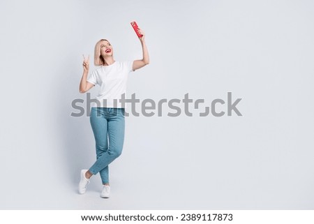 Full body photo of lovely woman wear stylish t-shirt jeans making selfie on smartphone show v-sign isolated on gray color background
