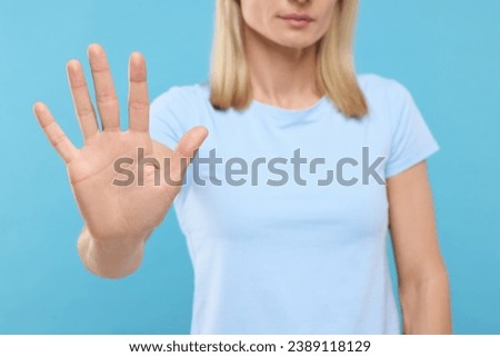 Woman showing stop gesture on light blue background, closeup