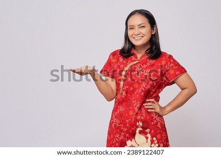 Smiling young Asian woman wearing a traditional cheongsam qipao dress showing empty space with hand on advertising isolated on white background. Happy Chinese New Year