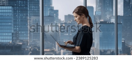 Caucasian Businesswoman Standing In Her Corner Office Next To Big Window With City View And Using Laptop Computer. Successful Business Manager Reviewing Tasks, Reading Emails. Royalty-Free Stock Photo #2389125283