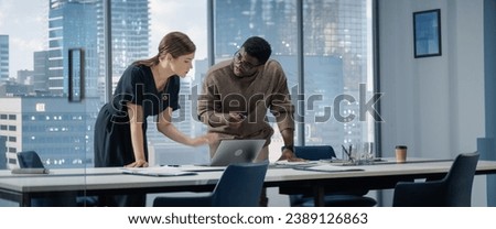 Successful Businesswoman Working on Top Floor Office Overlooking Big City. Female CEO of Humanitarian Investment Fund Talks To Black Male Investor And Discuss Graphs On Laptop. Royalty-Free Stock Photo #2389126863