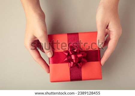 Red gift with red bow in female hands on grey background. Space for text. Top view