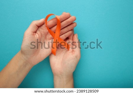 Hands holding orange color ribbon on blue background. Kidney Cancer Awareness, Leukemia disease, Skin cancer awareness, World Cancer Day. Healthcare or hospital and insurance concept.