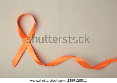 Orange ribbon on grey background . Healthcare and medicine concept. Multiple Sclerosis awareness. Leukemia awareness. Empty text space. Top view Royalty-Free Stock Photo #2389128511