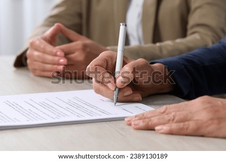 Signing document. Women at light wooden table indoors, closeup