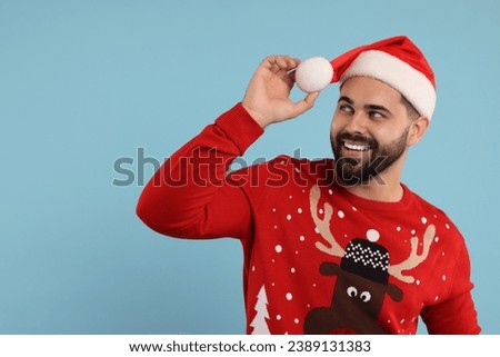 Happy young man in Christmas sweater and Santa hat on light blue background. Space for text