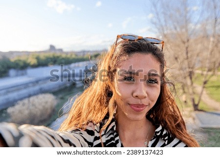 young latina taking a selfie with smart phone in a city park