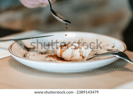 Detail shot of a spoon delicately drizzling sauce over a gyoza on a designer plate