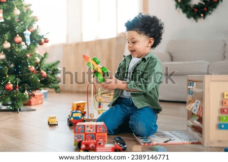 African american curly haired boy child on floor playing with christmas presents near tree in light room