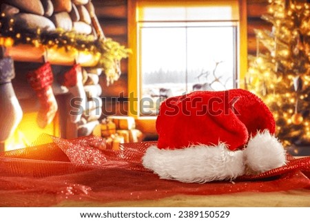 Red Santa Claus hat on board and fireplace in home interior. 