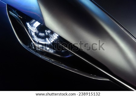 Predatory car headlight and hood of powerful sports grey car with blue glare on dark background Royalty-Free Stock Photo #238915132