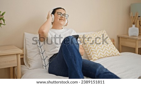 Young beautiful hispanic woman using smartphone dancing wearing headphones at bedroom