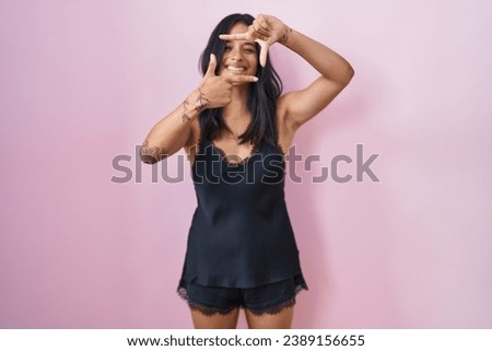 Brunette woman wearing black pajama smiling making frame with hands and fingers with happy face. creativity and photography concept. 