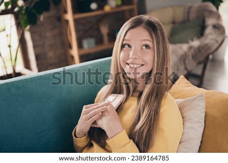 Portrait of beautiful cute lovely schoolgirl teenager dreaming holding new apple iphone 15 surprise from parents sitting divan at home