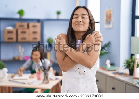 Young woman at art studio hugging oneself happy and positive, smiling confident. self love and self care  Royalty-Free Stock Photo #2389173083