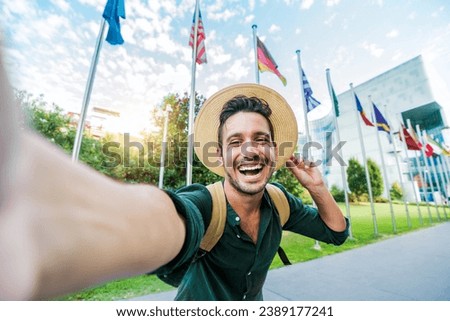 Happy tourist visiting financial district standing on city street - Young handsome traveler with hat and backpack enjoying summer vacation outside - Technology life style and summer vacations concept