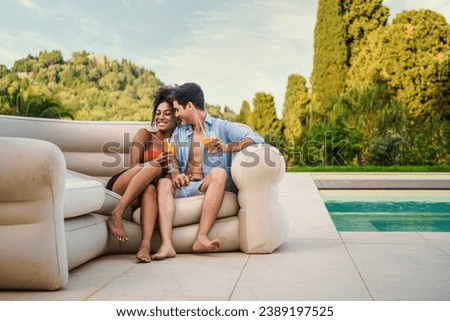 Couple sharing a romantic moment with refreshing drinks by the pool in a luxurious resort setting. Royalty-Free Stock Photo #2389197525