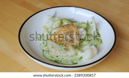 The cook prepares a dish with fish. Close-up professional chef in a restaurant kitchen serving a dish adding the last ingredient by hand. The male chef makes the composition of the dish for serving.