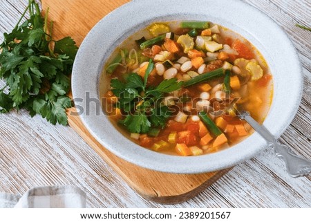 Minestrone white bean soup with seasonal summer vegetables, healthy vegan meal,  rustic wooden table, close up