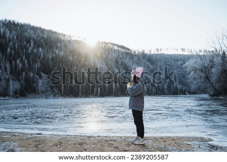 Yoga meditation in nature, girl practicing yoga in winter standing on the shore of a cold frozen lake, sunlight illuminates a man in the mountains. High quality photo