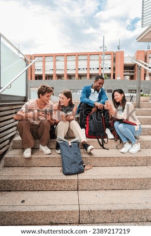 Vertical. Group of multiracial high school students talking on a staircase at university campus, using a tablet app and smartphone to do homework project after class. Friendly teenage people studying