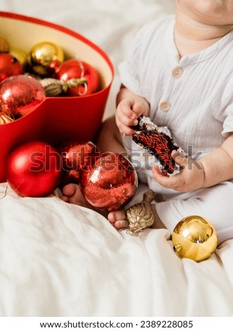 Close-up Christmas Baby in Santa Hat, Child holding christmas bauble near Present Gift Box over Holiday Lights background