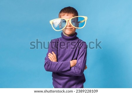 Cheerful little boy in big glasses express a surprised face isolated on blue background. Generation alpha and gen alpha children.