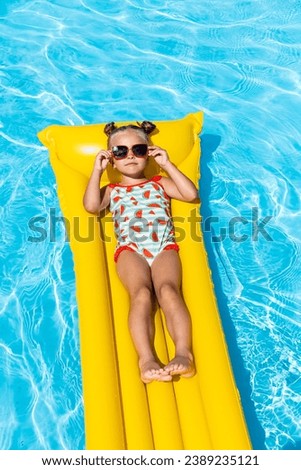 Cute little girl lying on inflatable mattress in swimming pool with blue water on warm summer day on tropical vacations. Summertime activities concept. Cute little girl sunbathing on air mattress Royalty-Free Stock Photo #2389235121