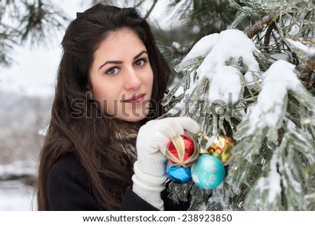 Young beauty woman decorates a fir tree with toys in outdoor