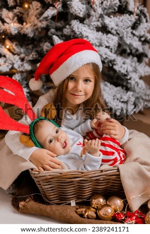 two little girls sisters in New Year's pajamas are sitting under the Christmas tree at home