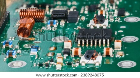 Closeup of surface mounted electronic components in radio-frequency circuits of TV tuner. Semiconductor microchip and air core coils with various small inductors, capacitors or resistors on green PCB. Royalty-Free Stock Photo #2389248075