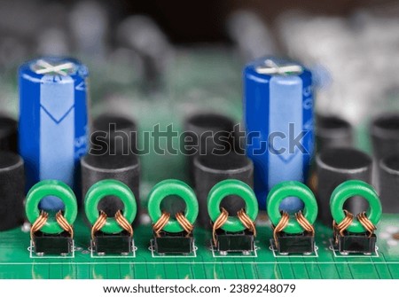 Closeup of toroidal core coils and blue electrolytic capacitors on green PCB. Row of transformer inductors on printed circuit board for audio or video signal galvanic isolation with blurry background. Royalty-Free Stock Photo #2389248079