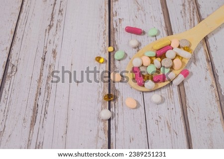 Assorted pharmaceutical medicine pills, tablets and capsules on wooden spoon.