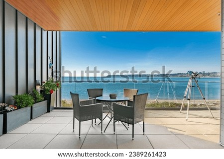 Ocean view from concrete deck with blue sky sunny day ocean front condo in pacific northwest looking toward White Rock BC Semaimoo peninsula patio furniture and telescope