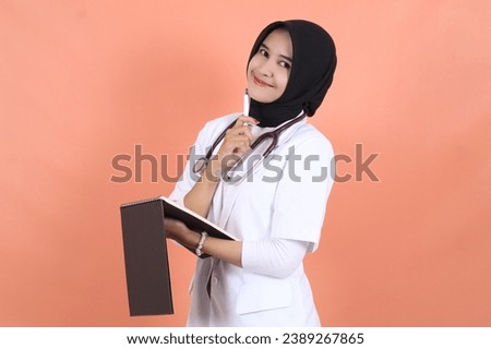 veiled female asian muslim doctor wearing white suit uniform with stethoscope, waist up and smiling with holding pen and notebook, got idea.