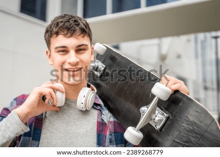 One man young adult caucasian teenager stand outdoor with skateboard on his shoulder and headphones posing portrait looking to the camera happy confident wear shirt casual real person copy space